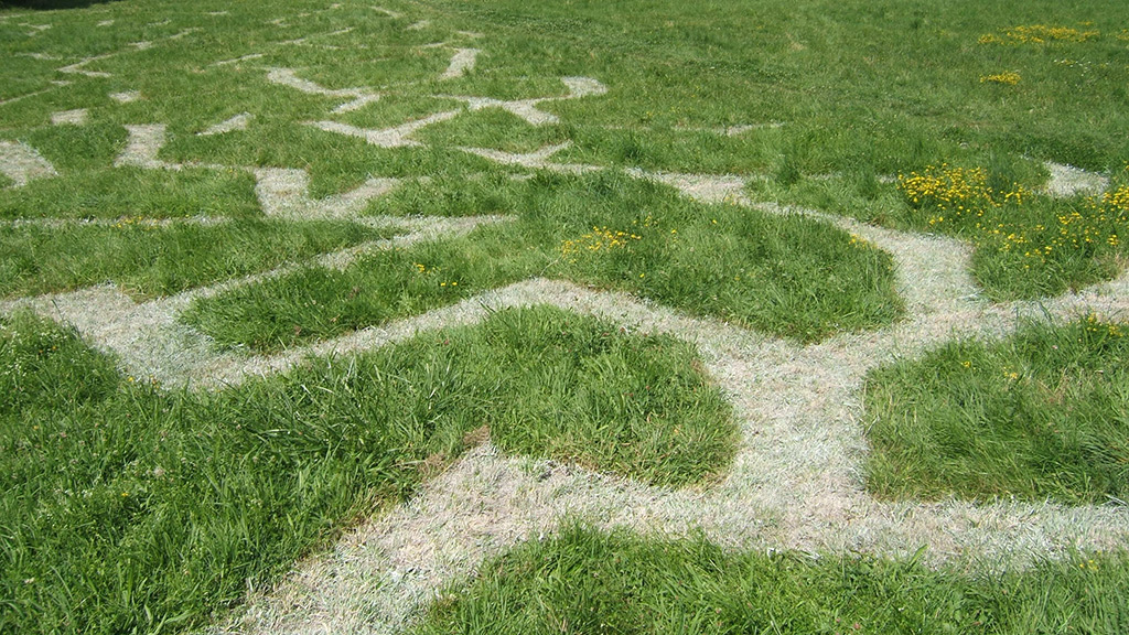 Installation en extérieure d'un dédale tracé au sol dans l'herbe tel un labyrinthe.