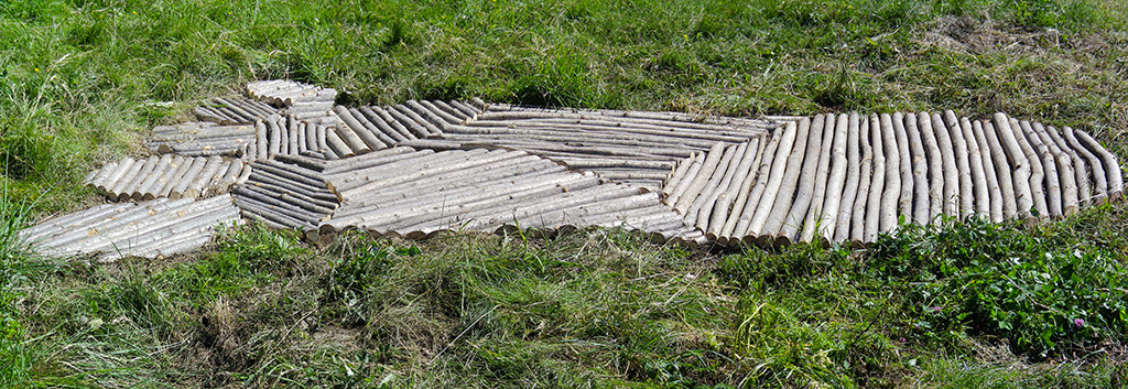 Installation dans la campagne faite de bois créant une trace géante laissée au sol.  