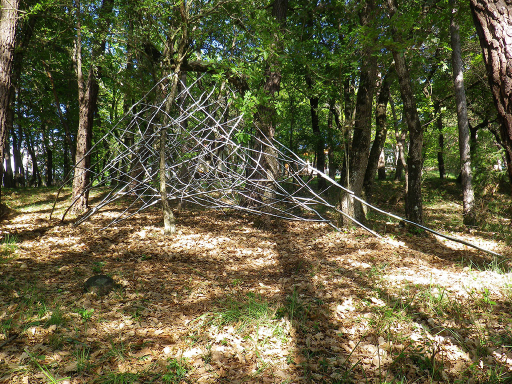 Installation in situ de l'artiste Anne Mangeot dans une forêt: grande structure en branches tissées entre les arbres.