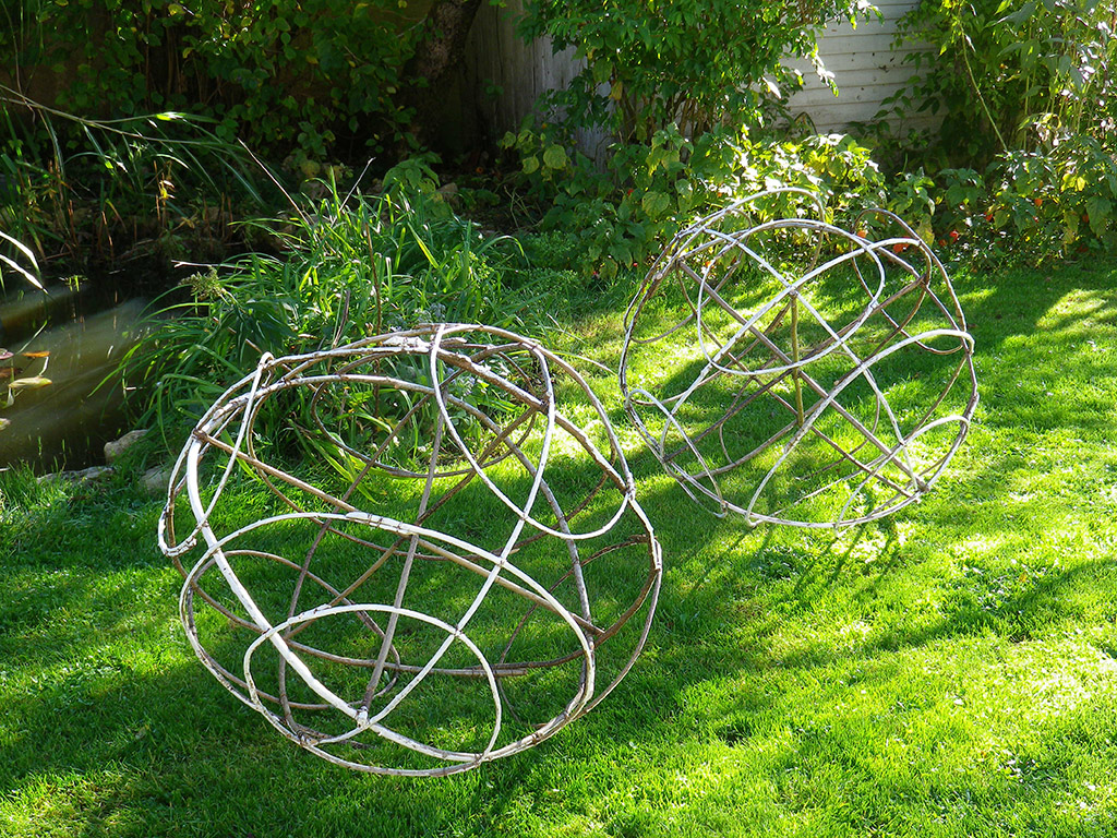 Structures de bois tressés formants de grandes boules dans un jardin, une installation de l'artiste Anne Mangeot.