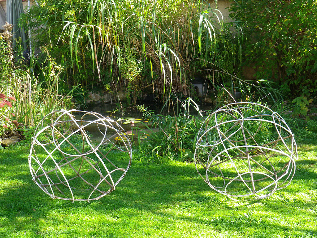 Structures de bois tressés formants de grandes boules dans un jardin.