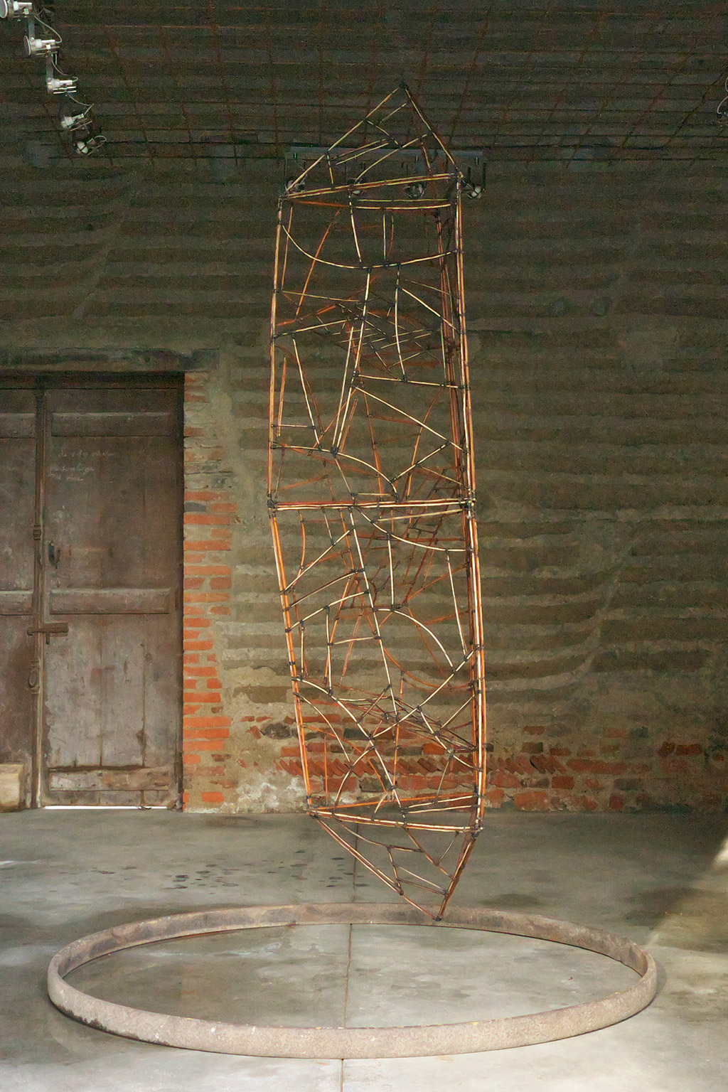 Une sculpture d'Anne Mangeot est exposée suspendue, devant un mur de brique.