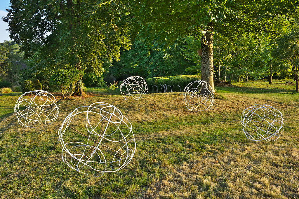 Installation de l'artiste Anne Mangeot, des sphères trônent au milieu d'un parc et sous des arbres.