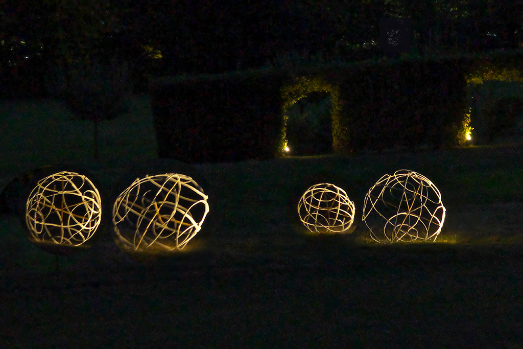 Immobilisées dans leur mouvement, des boules schématiques faites de branchages sont abandonnées sur un terrain herbeux, une installation d'Anne Mangeot.